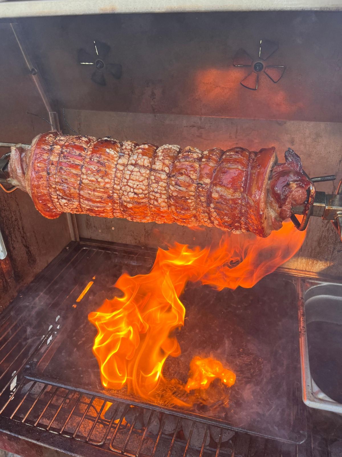 Rollbraten aus Schweinebauch am Drehspieß, knusprige Kruste über offener Flamme
