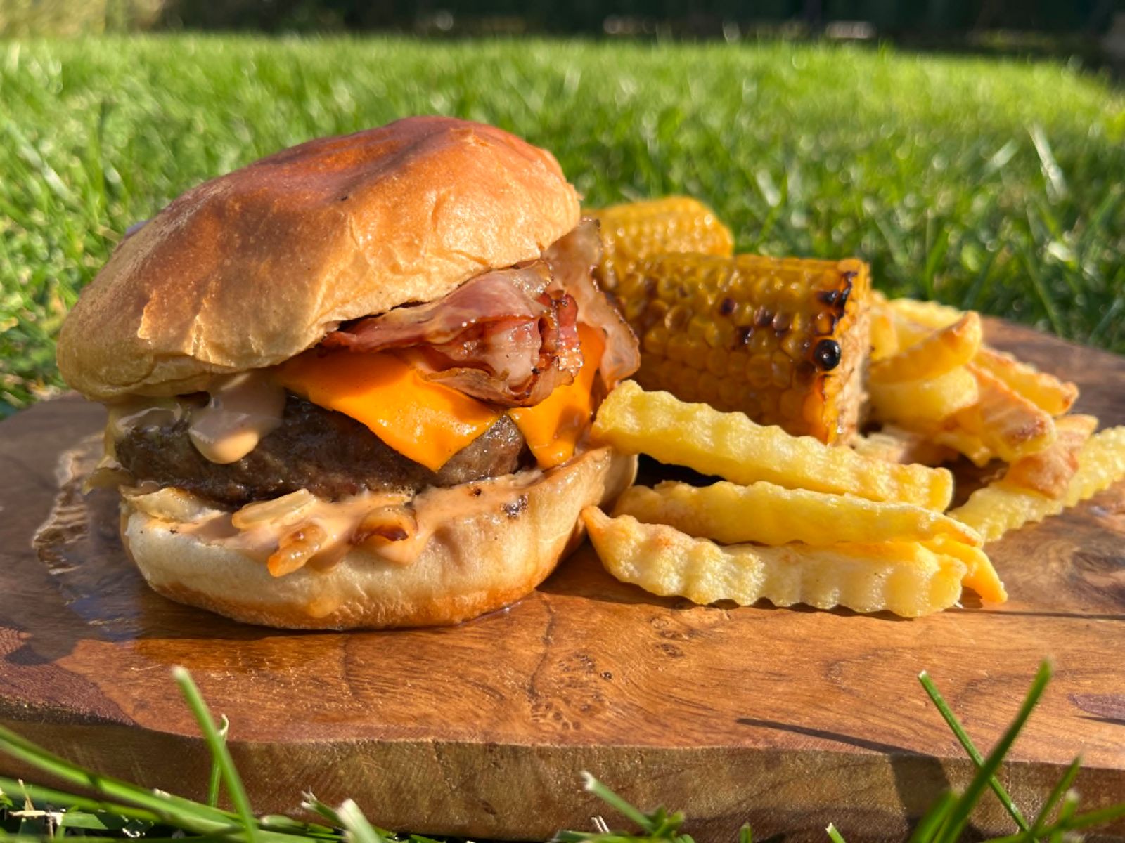 LF Burger mit Bacon, Cheddar und Pommes auf Holzbrett