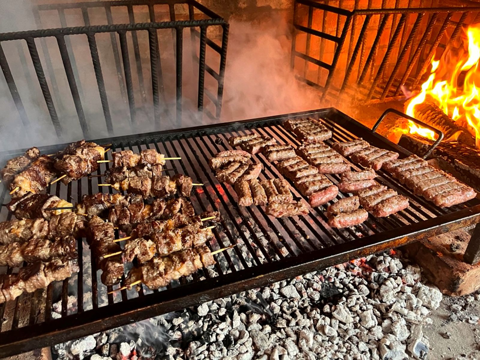 Fleischspieße und Ćevapi auf dem Holzkohlegrill mit offener Flamme